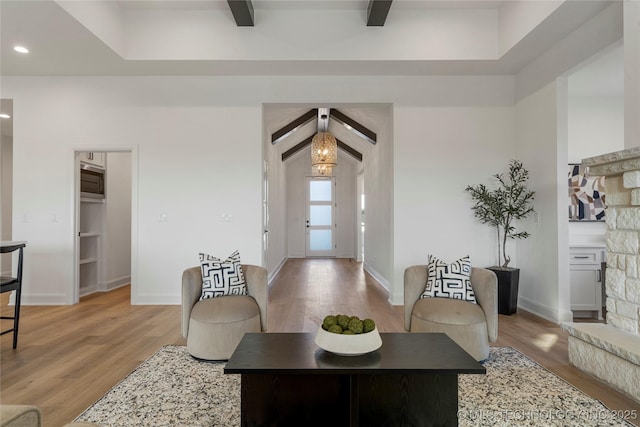 living room with beam ceiling, a fireplace, a chandelier, and light hardwood / wood-style flooring