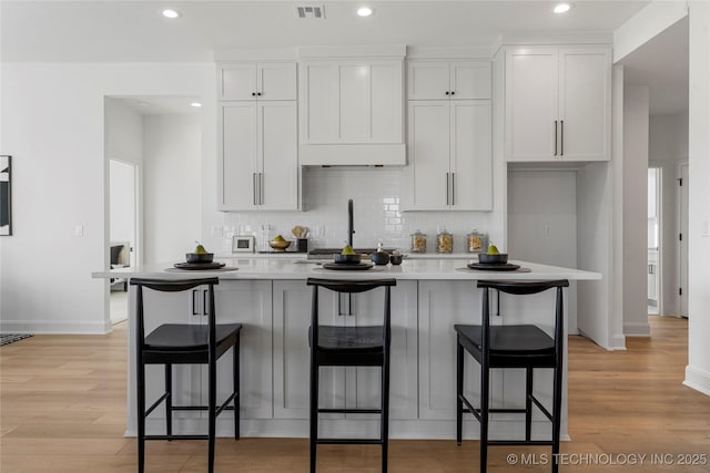 kitchen with a breakfast bar area, white cabinetry, a kitchen island with sink, and light hardwood / wood-style floors