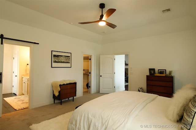 bedroom featuring light carpet, a walk in closet, ensuite bath, ceiling fan, and a barn door