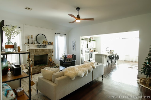 living room with ceiling fan, dark wood-type flooring, sink, a fireplace, and lofted ceiling