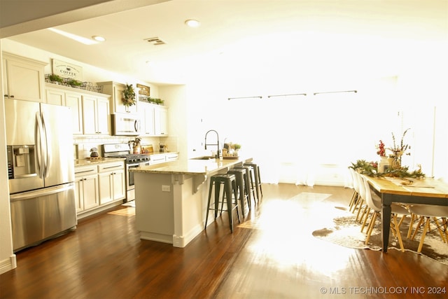 kitchen with appliances with stainless steel finishes, a center island with sink, dark wood-type flooring, and sink