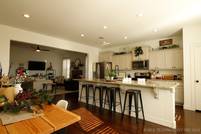 kitchen with light stone countertops, stainless steel appliances, a kitchen breakfast bar, dark hardwood / wood-style floors, and an island with sink