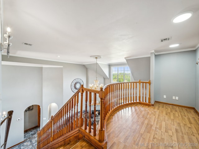 staircase featuring wood-type flooring, crown molding, and a notable chandelier