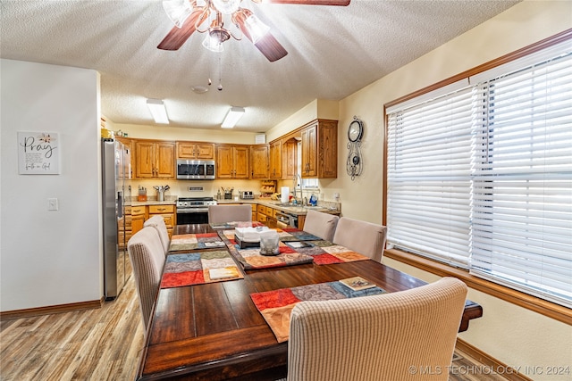 dining space with ceiling fan, sink, light wood-type flooring, and a textured ceiling