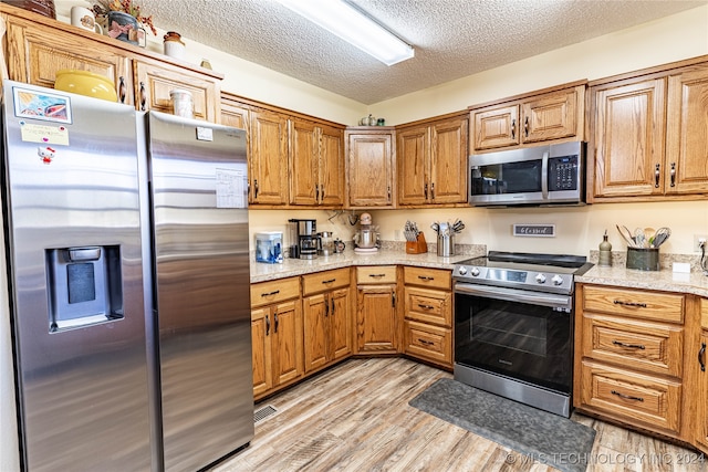 kitchen with light stone counters, a textured ceiling, stainless steel appliances, and light hardwood / wood-style flooring