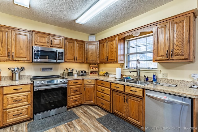 20515 S 4450, Vinita, OK 74301 - kitchen featuring appliances with stainless steel finishes, a sink, light wood-type flooring, brown cabinetry, and a textured ceiling