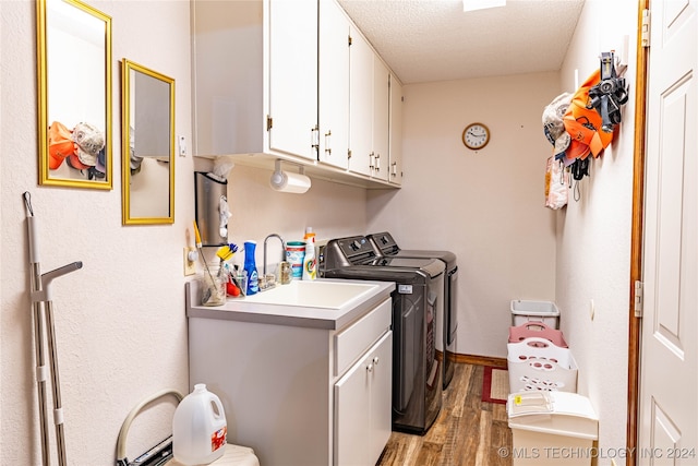 washroom featuring a textured ceiling, light wood-type flooring, washer and dryer, and cabinets