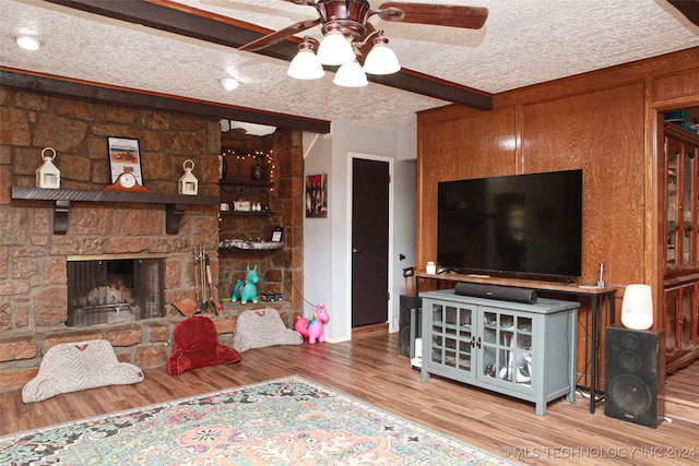 living room with hardwood / wood-style floors, a stone fireplace, ceiling fan, a textured ceiling, and beam ceiling