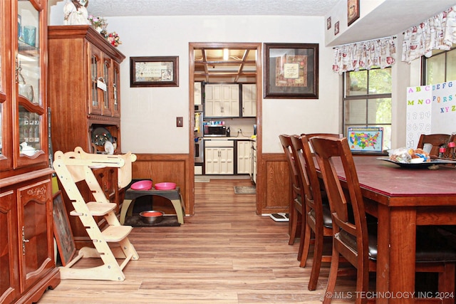 dining room featuring a textured ceiling, light hardwood / wood-style flooring, and wooden walls