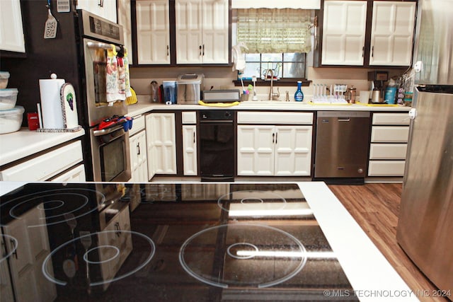 kitchen with wood-type flooring, appliances with stainless steel finishes, white cabinets, and sink