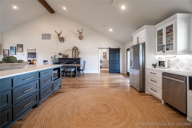 kitchen featuring stainless steel appliances, white cabinets, light hardwood / wood-style floors, a barn door, and beam ceiling