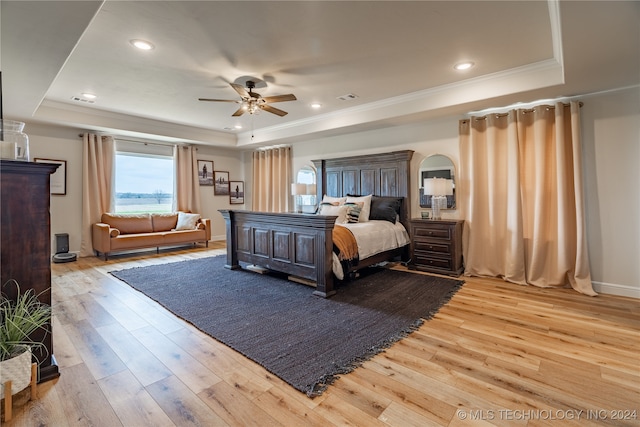 bedroom featuring light hardwood / wood-style floors, a tray ceiling, ornamental molding, and ceiling fan