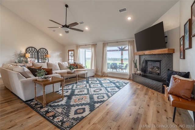 living room with ceiling fan, light wood-type flooring, a fireplace, and high vaulted ceiling