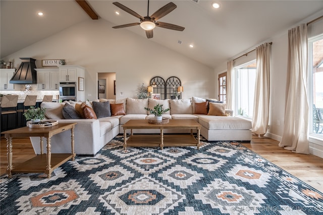 living room with beam ceiling, high vaulted ceiling, ceiling fan, and light hardwood / wood-style flooring