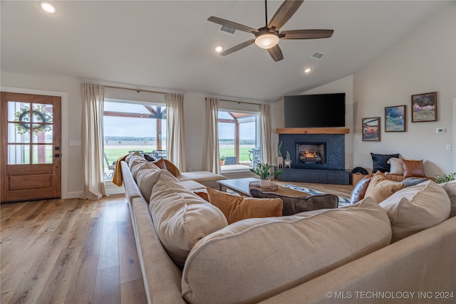 living room with light wood-type flooring, a tiled fireplace, lofted ceiling, and a healthy amount of sunlight