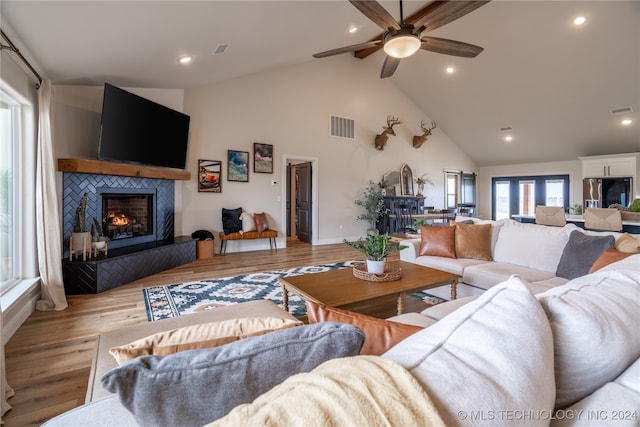 living room with high vaulted ceiling, a fireplace, ceiling fan, and light hardwood / wood-style flooring