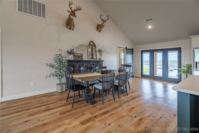 dining room with light wood-type flooring, a barn door, and high vaulted ceiling