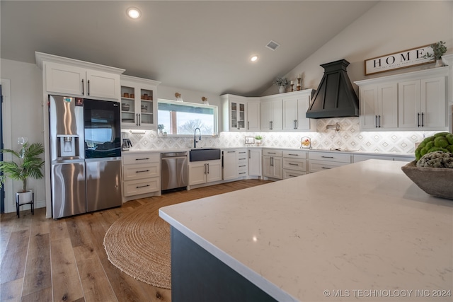 kitchen with hardwood / wood-style floors, stainless steel appliances, custom range hood, white cabinetry, and vaulted ceiling