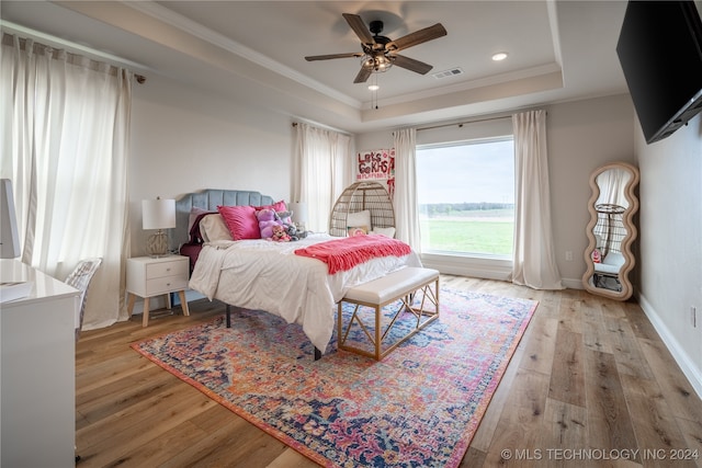 bedroom with ceiling fan, a raised ceiling, crown molding, and light hardwood / wood-style floors