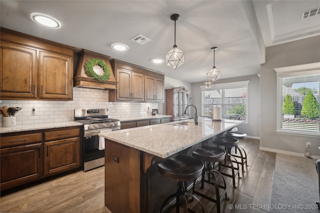 kitchen with light hardwood / wood-style flooring, a center island with sink, a kitchen breakfast bar, and stainless steel range with gas stovetop