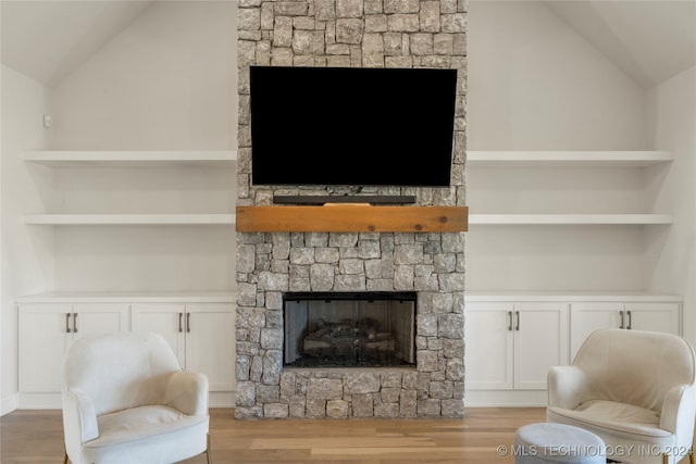 living room featuring lofted ceiling, built in features, light hardwood / wood-style floors, and a fireplace