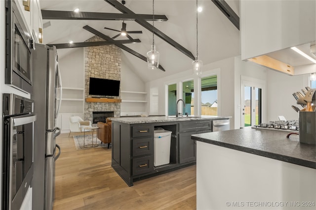 kitchen with beam ceiling, a kitchen island with sink, stainless steel appliances, a fireplace, and light hardwood / wood-style floors