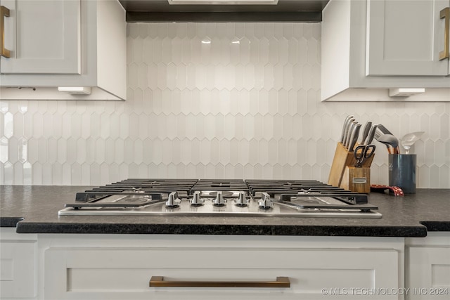 kitchen featuring range hood, backsplash, stainless steel gas cooktop, and white cabinetry