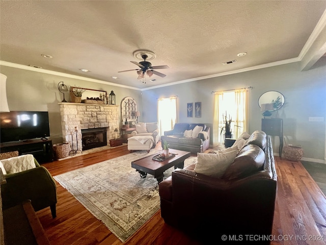 living room featuring ceiling fan, a stone fireplace, hardwood / wood-style floors, crown molding, and a textured ceiling