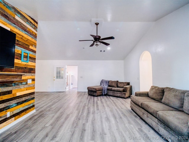 living room with ceiling fan, light wood-type flooring, wood walls, and high vaulted ceiling