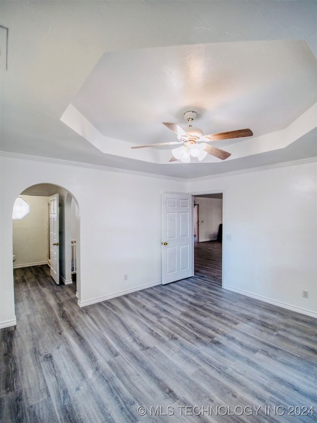 empty room with a raised ceiling, wood-type flooring, crown molding, and ceiling fan