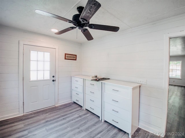 kitchen featuring white cabinets, light hardwood / wood-style flooring, wooden walls, and ceiling fan