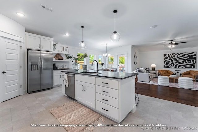 kitchen featuring dark countertops, a sink, a kitchen island with sink, appliances with stainless steel finishes, and ceiling fan with notable chandelier