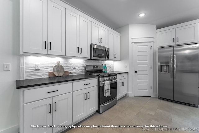 kitchen with light tile patterned floors, tasteful backsplash, dark countertops, appliances with stainless steel finishes, and white cabinets