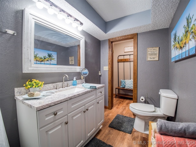 bathroom featuring wood-type flooring, vanity, toilet, and a textured ceiling