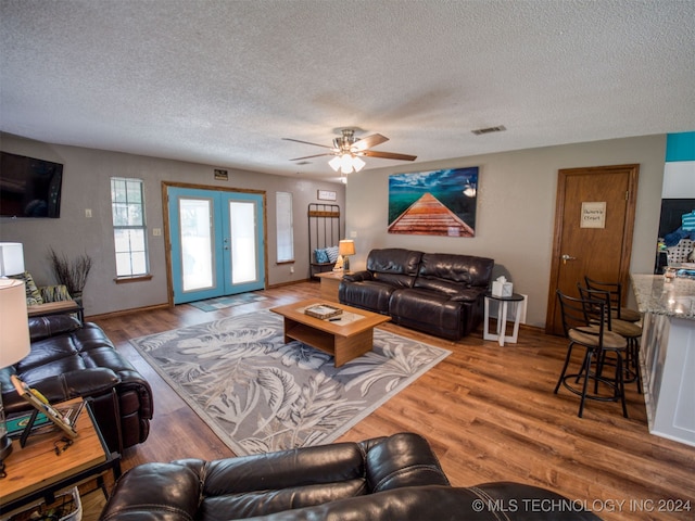 living room with ceiling fan, wood-type flooring, french doors, and a textured ceiling