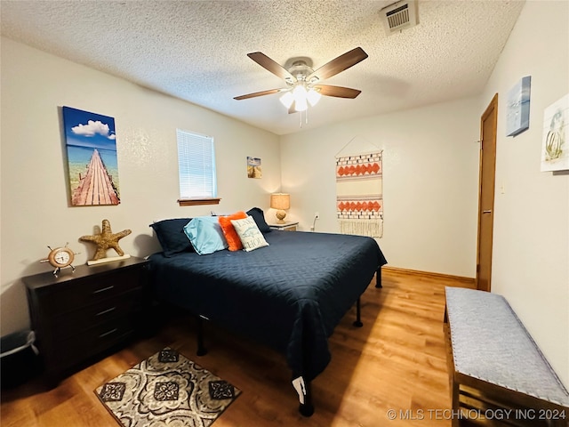 bedroom with ceiling fan, wood-type flooring, and a textured ceiling