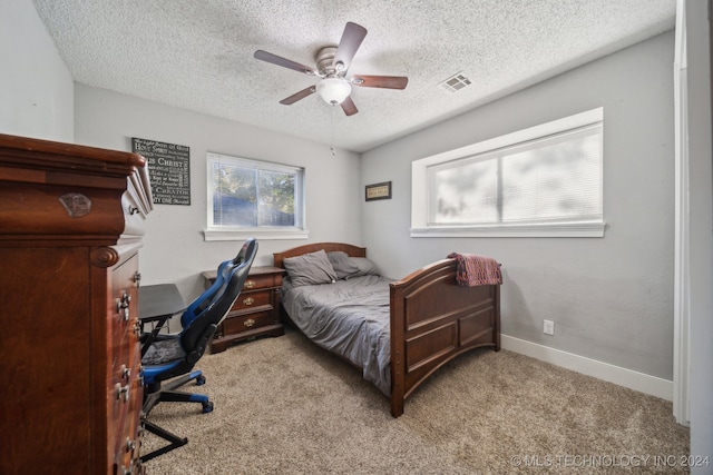 bedroom with a textured ceiling, multiple windows, light colored carpet, and ceiling fan