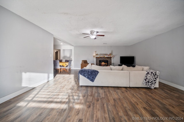 living room featuring dark wood-type flooring, a fireplace, a textured ceiling, and ceiling fan