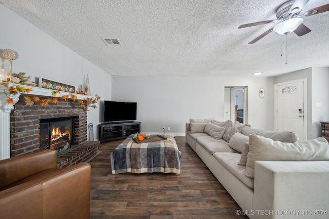 living room featuring ceiling fan, a textured ceiling, a brick fireplace, and dark hardwood / wood-style floors