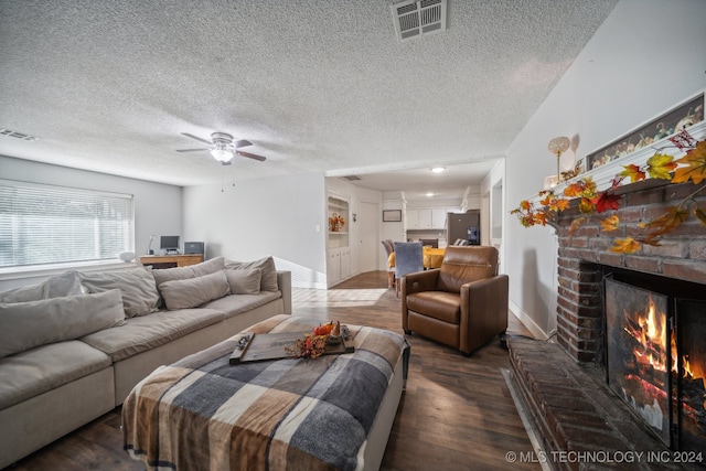 living room with a textured ceiling, a brick fireplace, dark hardwood / wood-style floors, and ceiling fan