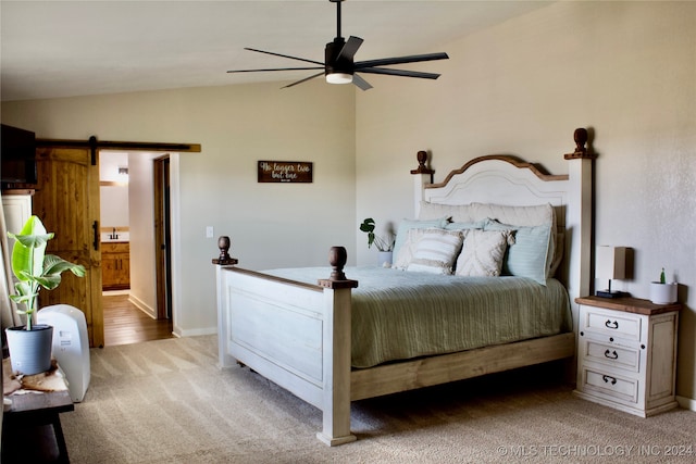 bedroom with connected bathroom, lofted ceiling, a barn door, light colored carpet, and ceiling fan