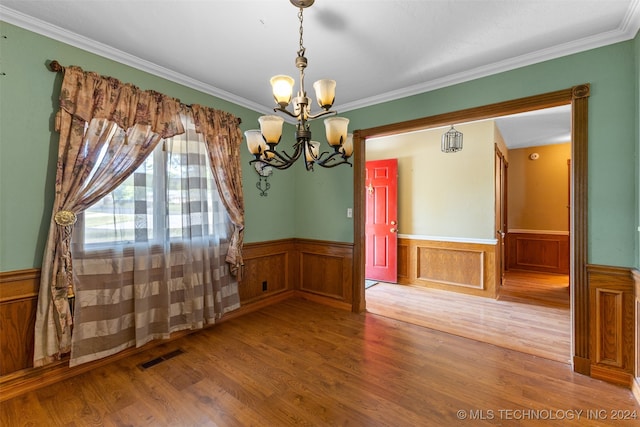 unfurnished dining area featuring ornamental molding, wood-type flooring, and an inviting chandelier