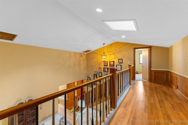 corridor featuring an inviting chandelier, lofted ceiling, and light wood-type flooring