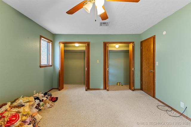 unfurnished bedroom with light carpet, two closets, and ceiling fan