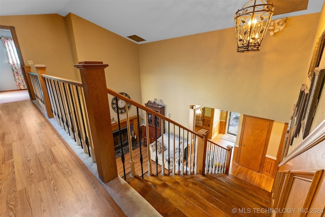 stairs featuring vaulted ceiling, an inviting chandelier, and hardwood / wood-style floors