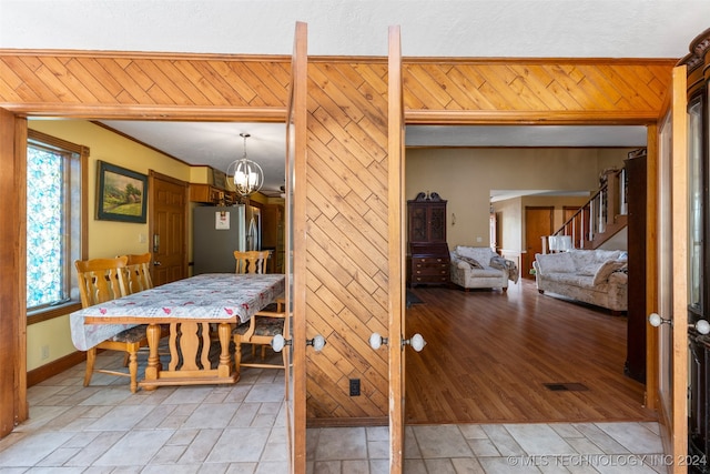 dining room featuring an inviting chandelier, light hardwood / wood-style flooring, wood walls, and crown molding