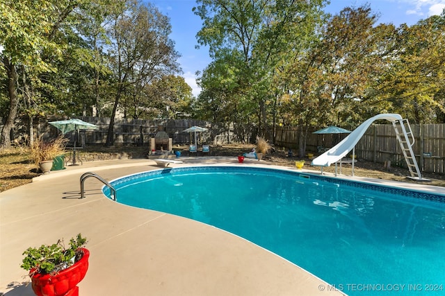 view of pool featuring a patio, a water slide, and a diving board