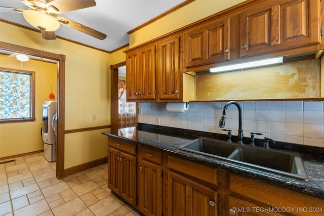 kitchen with tasteful backsplash, washer / clothes dryer, sink, dark stone countertops, and crown molding