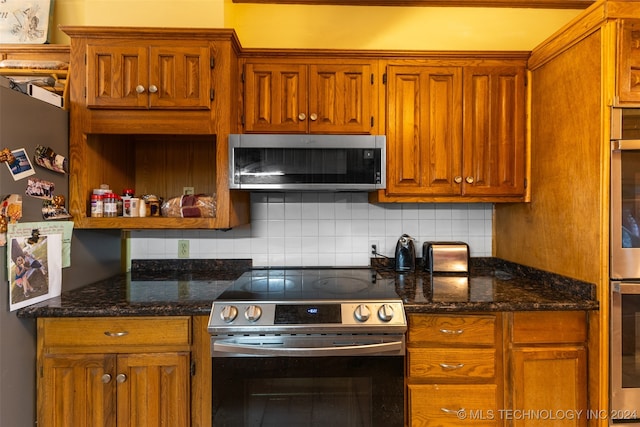 kitchen with appliances with stainless steel finishes, dark stone countertops, and tasteful backsplash