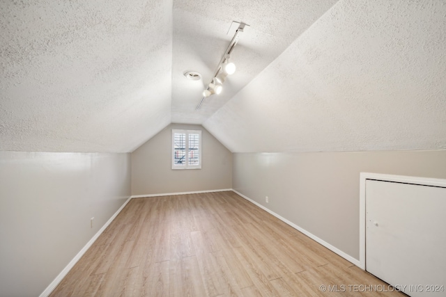 additional living space with a textured ceiling, light wood-type flooring, and vaulted ceiling